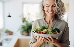 Woman smiling while holding large bowl filled with salad