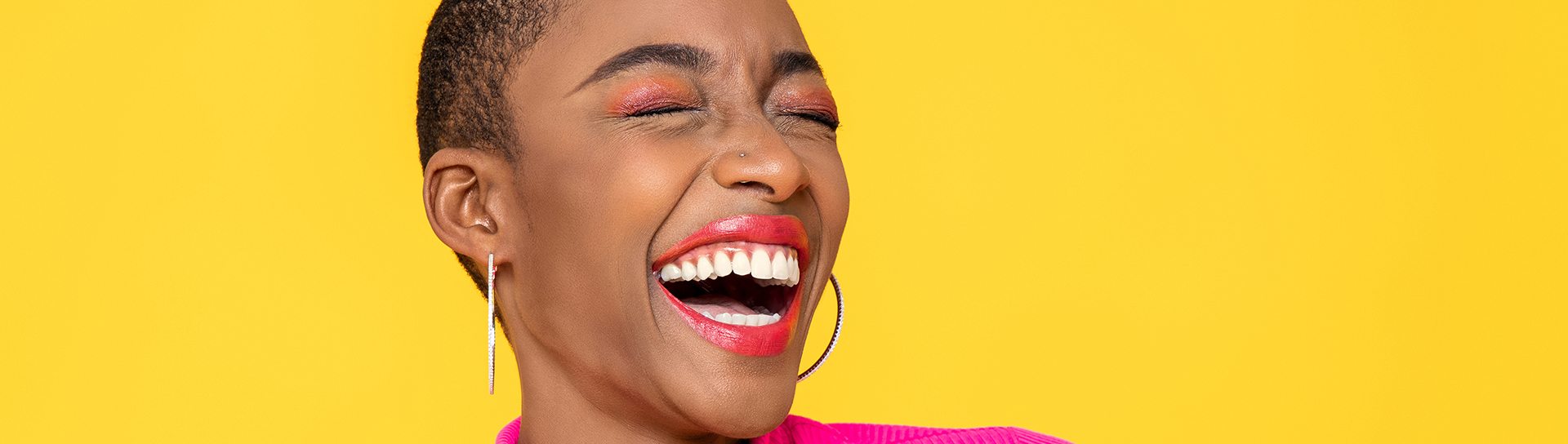 Woman in pink sweater laughing with eyes closed with yellow background