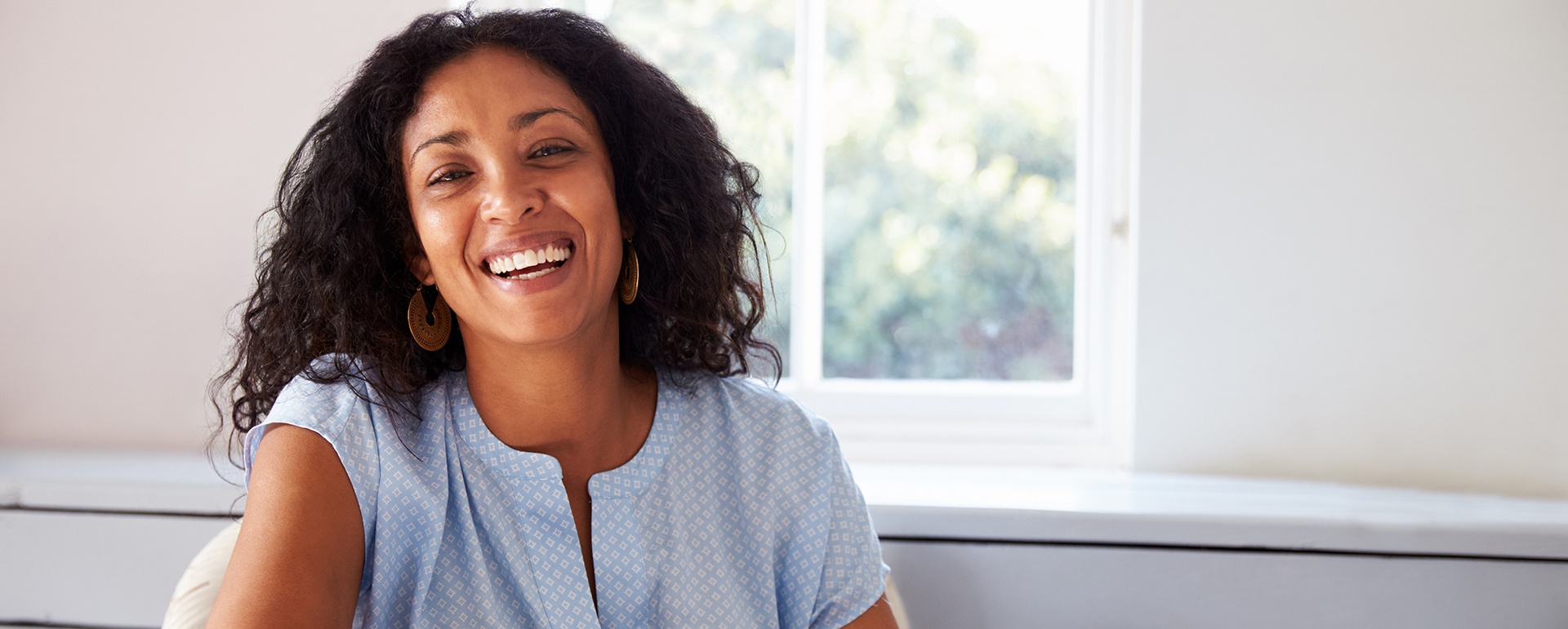 Woman smiling while sitting on chair next to window